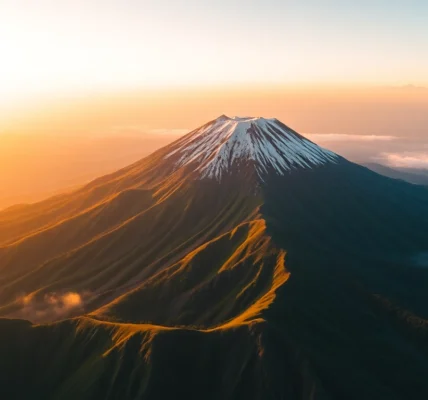 A stunning sunrise view of Mount Rinjani's crater rim with lush greenery and mist in the valleys below.